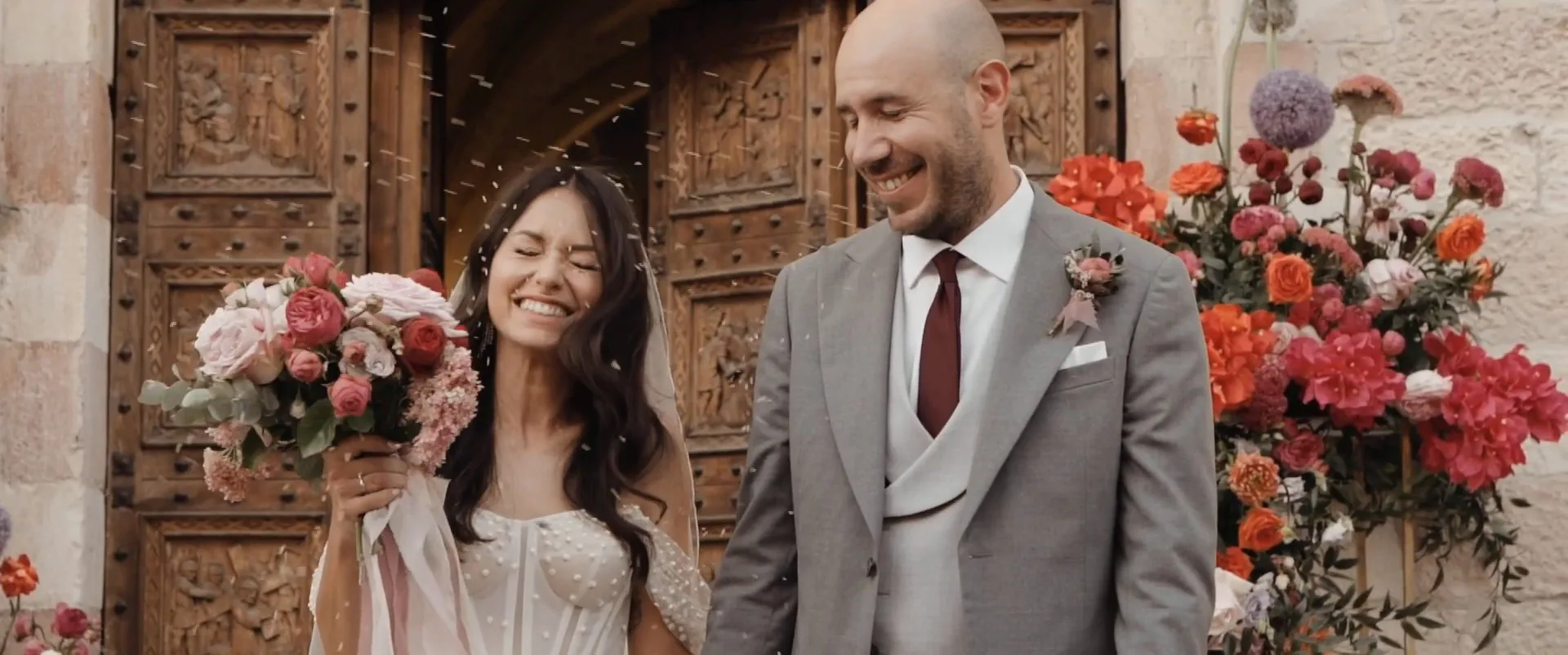 Edoardo e Gloria sorridono davanti al portale fiorito, fotogramma dal loro film