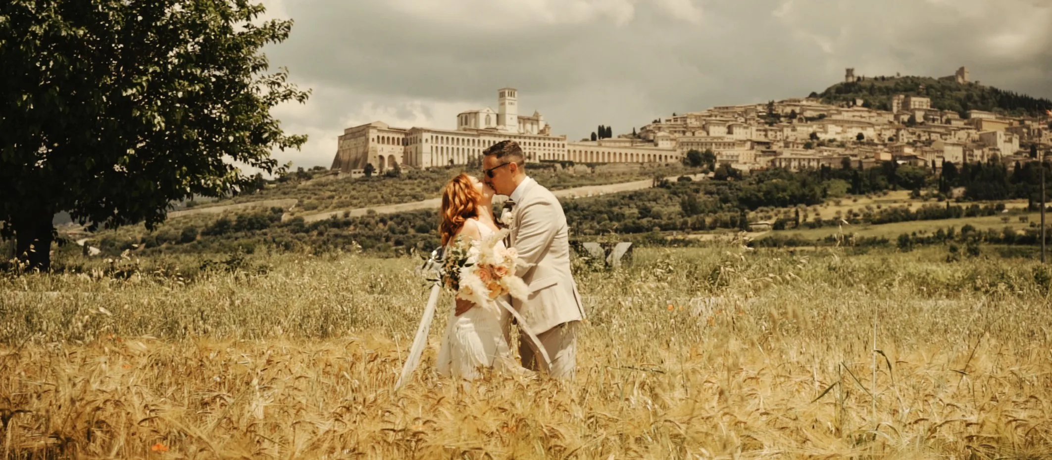 James e Stacey camminano nel grano con Assisi sullo sfondo