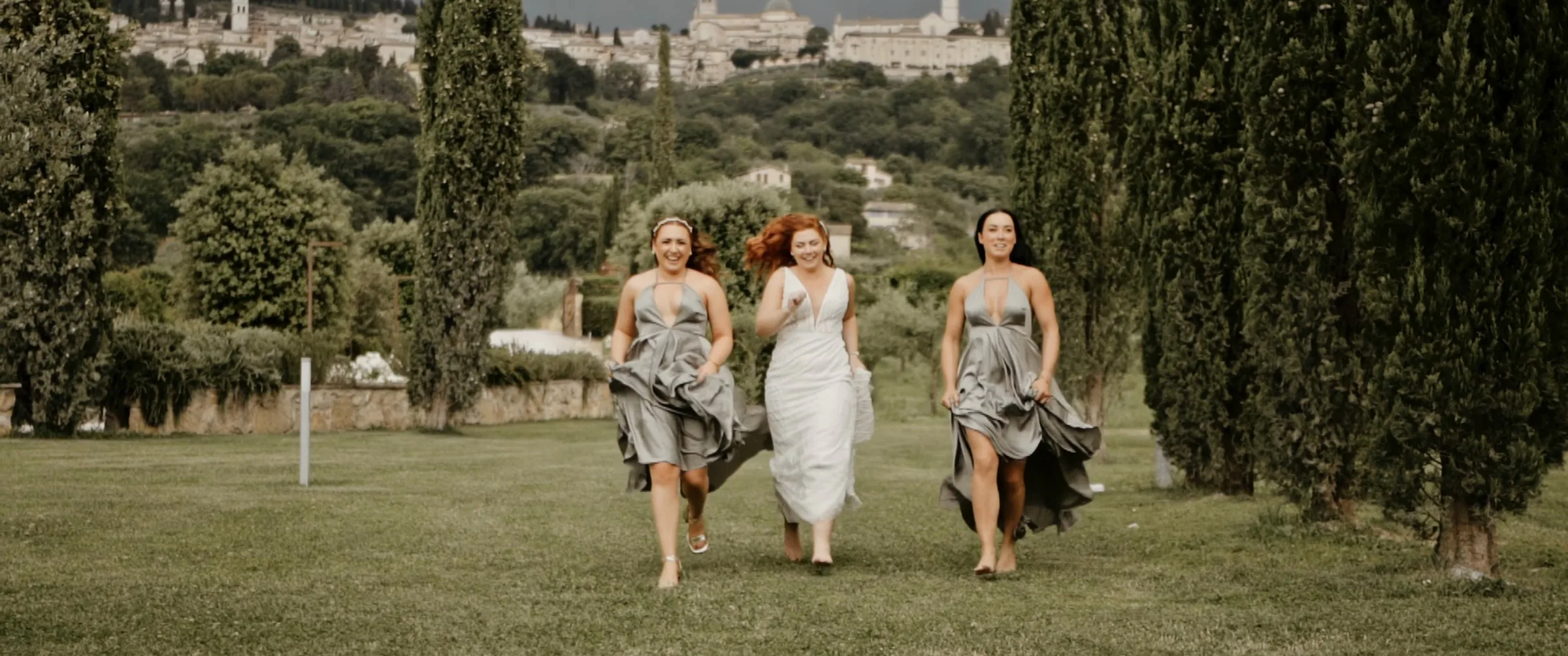 Le damigelle corrono nel giardino tra i cipressi alla Tenuta di San Masseo, con Assisi sullo sfondo, fotogramma dal film di James e Stacey